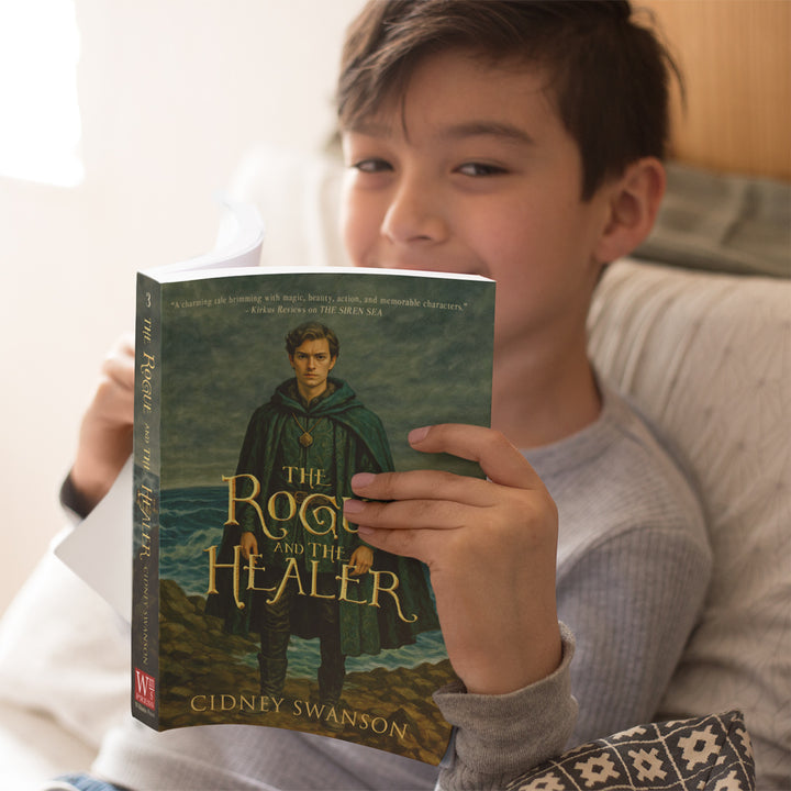 Smiling boy reading The Rogue and the Healer by Cidney Swanson — clean YA fantasy for ages 12+, third in the Five Kingdoms Chronicles.