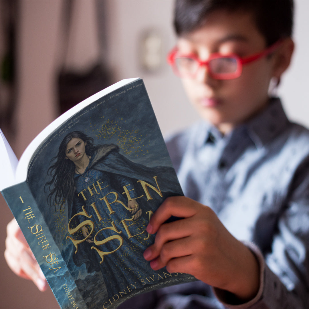 A boy reading The Siren Sea by Cidney Swanson — clean YA fantasy for ages 12+, first in the Five Kingdoms Chronicles.
