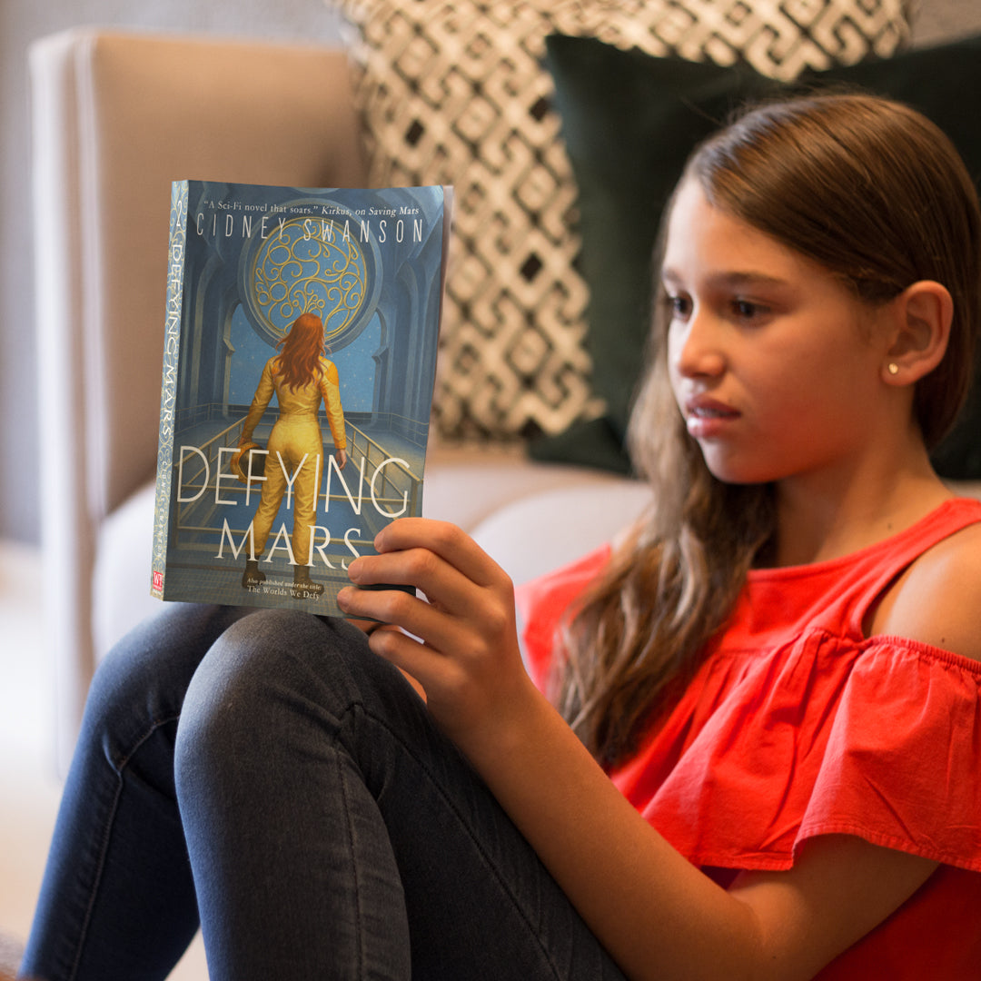 Girl reading Defying Mars by Cidney Swanson — clean YA sci-fi for ages 10+, second in the Saving Mars series.