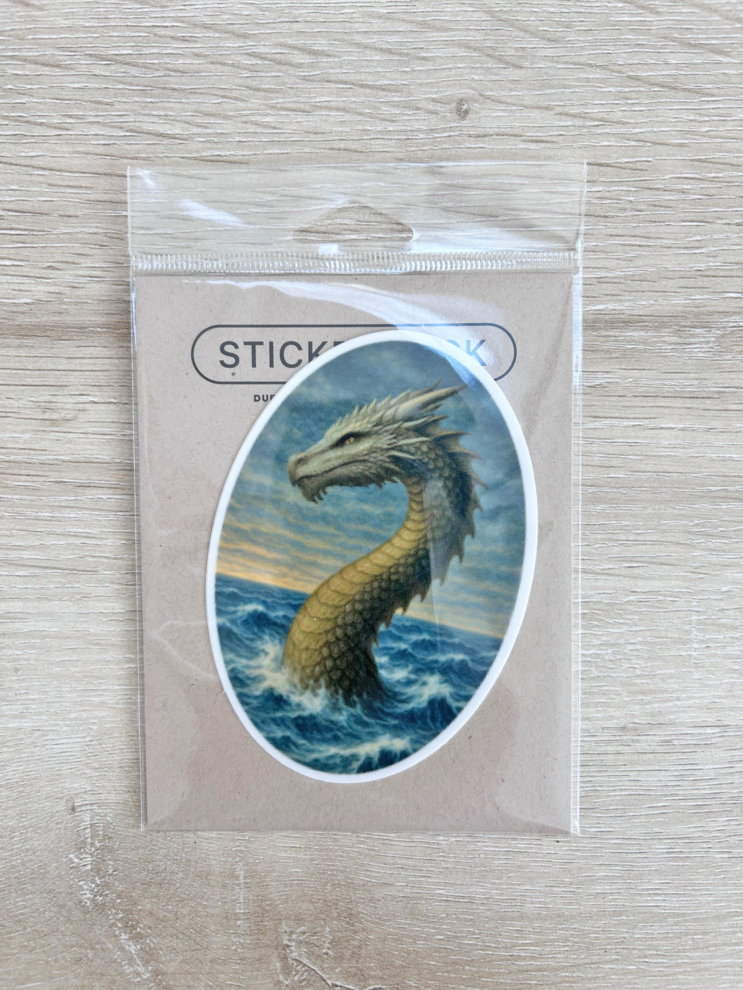 Sticker of the Water Worm Gwenllian shown in plastic packaging on a whitened wooden surface