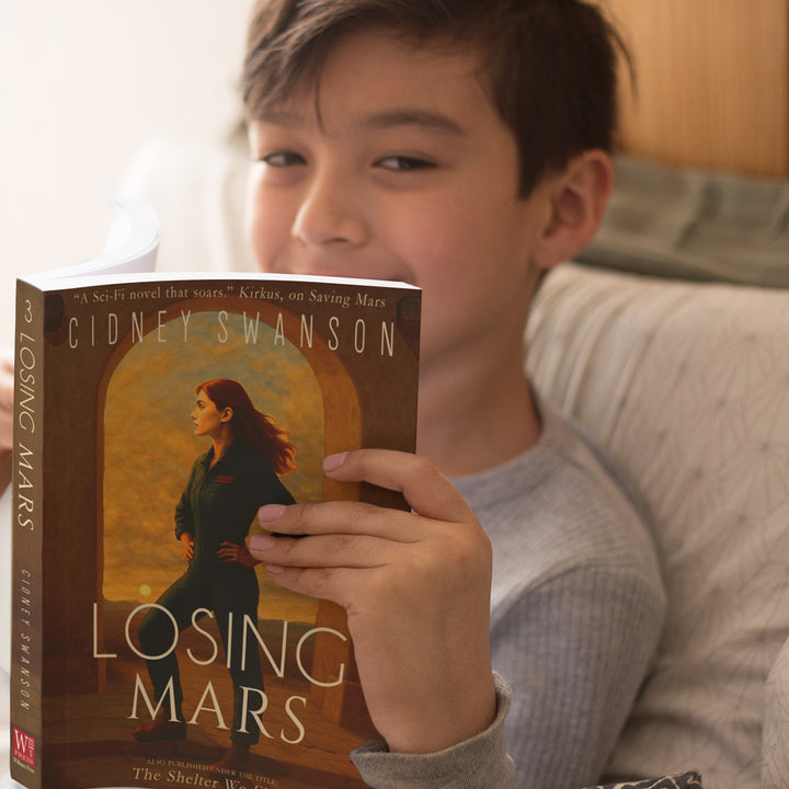 smiling boy reading Losing Mars by Cidney Swanson — clean YA sci-fi for ages 10+, third in the Saving Mars series.
