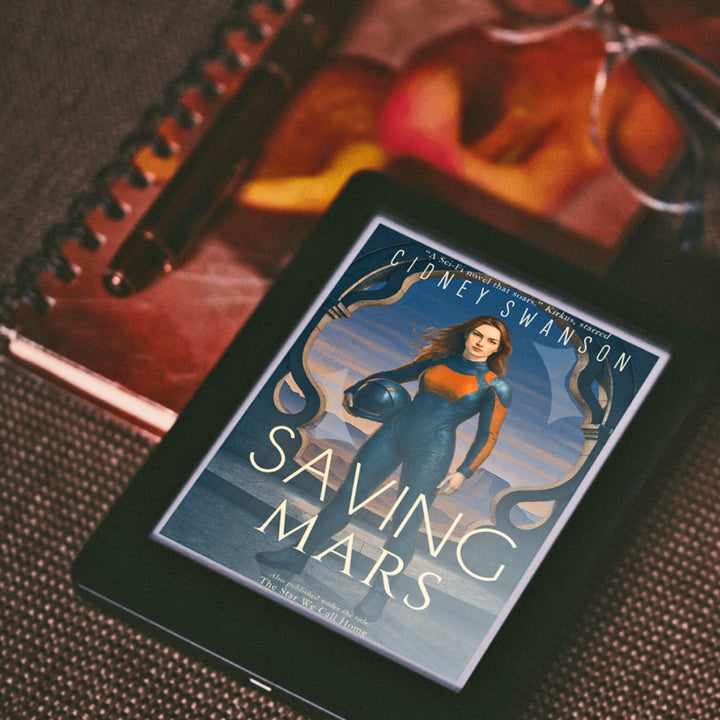 Saving Mars by Cidney Swanson — ebook on desk with notebook, clean YA sci-fi.