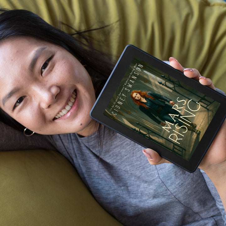 Young woman holds eBook of Mars Rising by Cidney Swanson | clean YA sci-fi for ages 10+, part of the Saving Mars series.