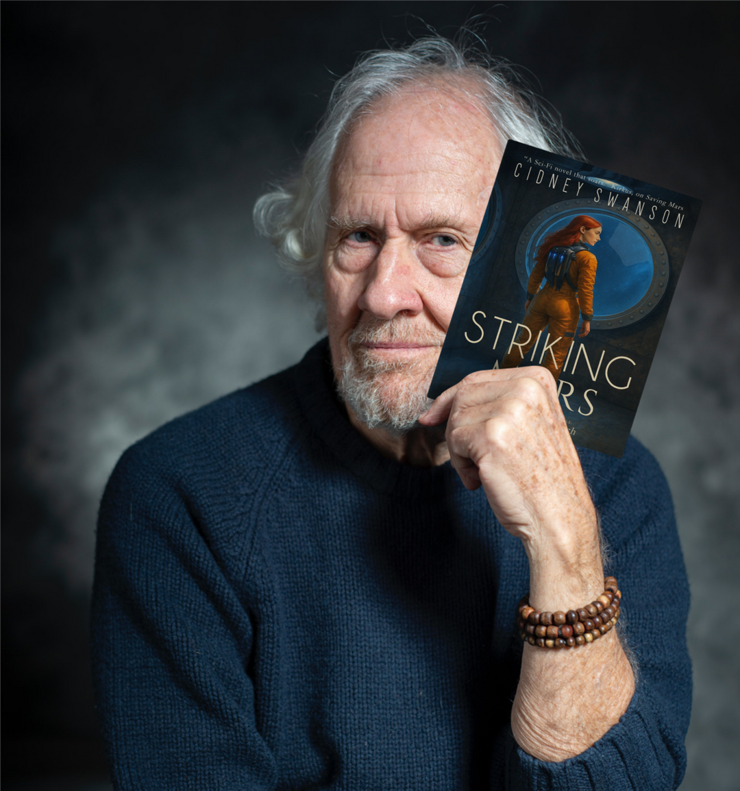 A hip grandfather holding Striking Mars by Cidney Swanson — clean YA sci-fi for ages 10+, fifth in the Saving Mars series