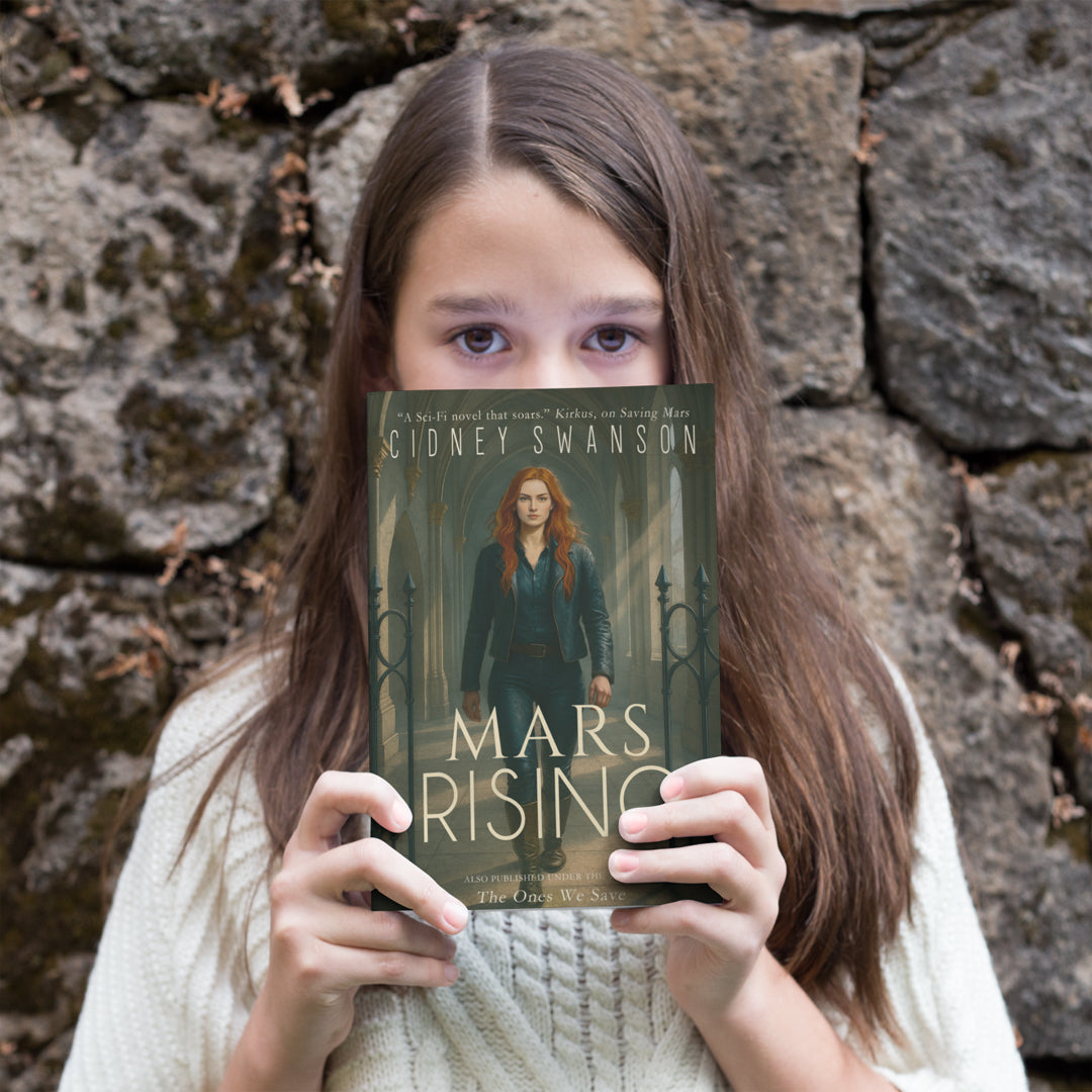 A young teen holds a copy of Mars Rising by Cidney Swanson — clean YA sci-fi for ages 10+, final book in the Saving Mars series..